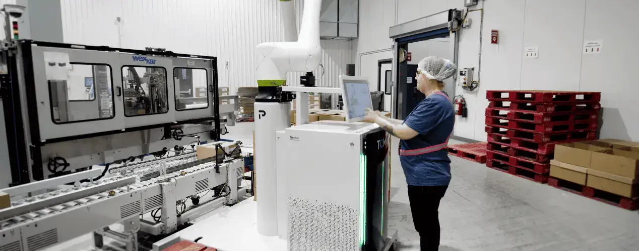Operator supervising a TOMA cobot palletizer that takes over heavy, repetitive tasks to reduce labor shortages on the line